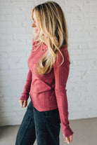 Woman wearing a red sweater and dark jeans against a white brick wall.