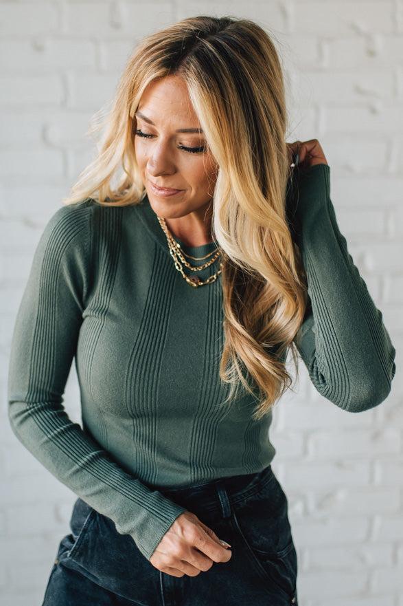 Woman wearing a green ribbed sweater against a white brick wall