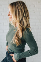 Woman wearing a green ribbed sweater against a white brick wall