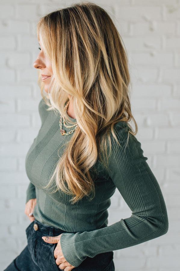 Woman wearing a green ribbed sweater against a white brick wall