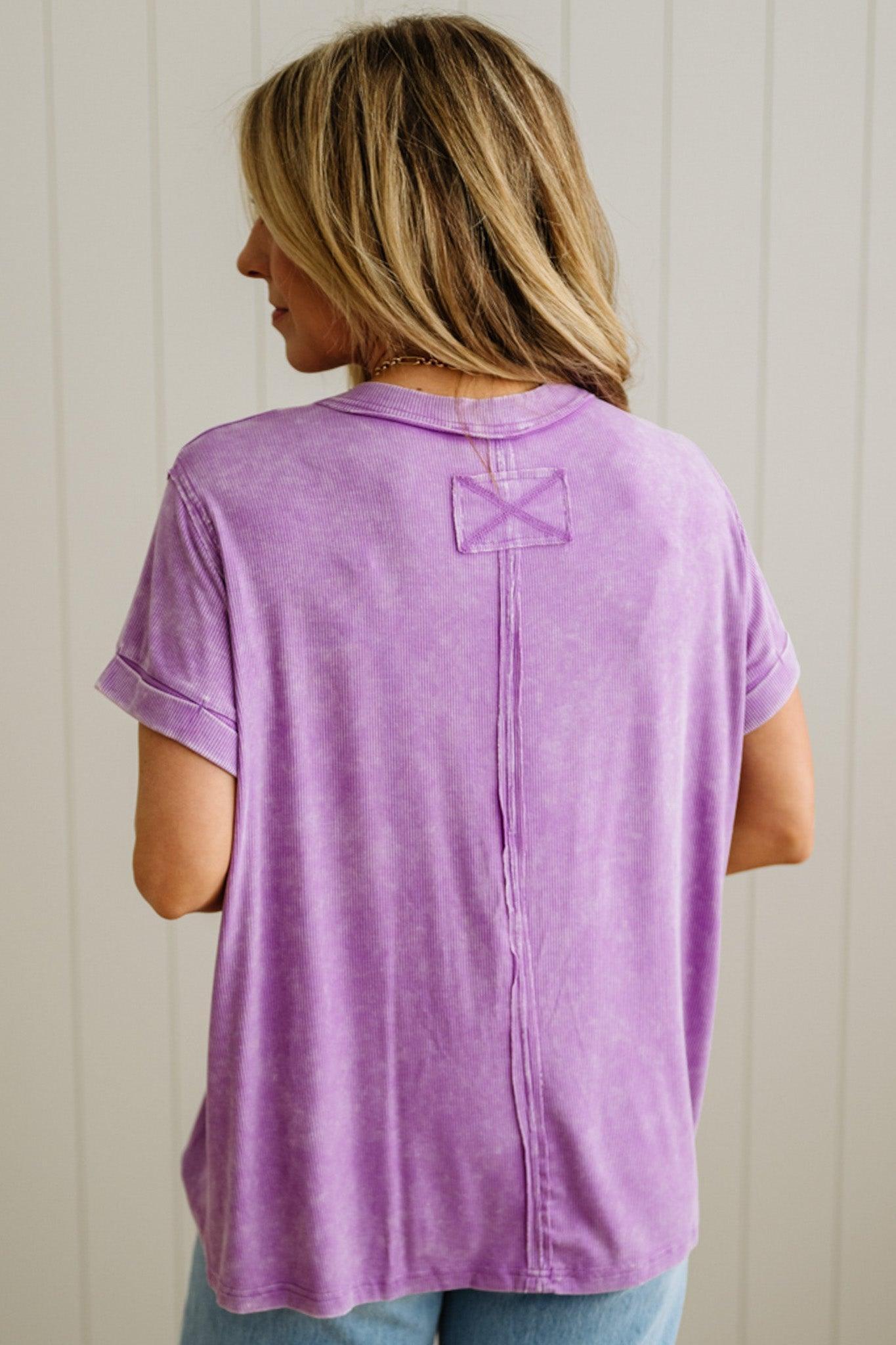 Person wearing a purple shirt with a decorative back bow against a white paneled wall.