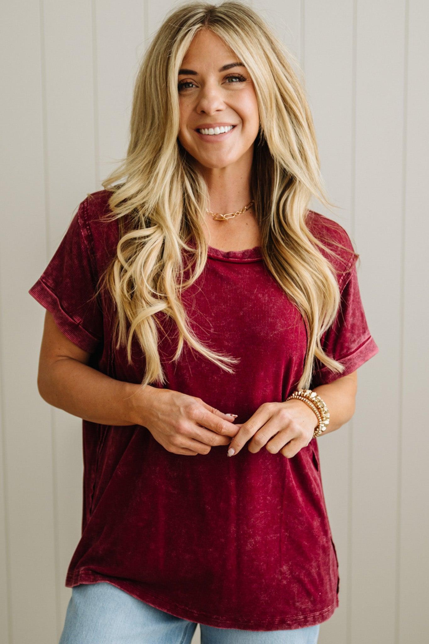 Woman wearing a maroon top and light blue jeans against a neutral background