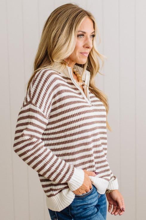 BLONDE WOMAN IN DARK JEANS STANDING IN A BRIGHTLY LIT STUDIO WITH LIGHT WOOD FLOORS AND A PANELED BACKDROP. SHE IS WEARING A CHUNKY NECKLACE AND QUARTER ZIP STRIPES SWEATER IN CREAM AND MOCHA.