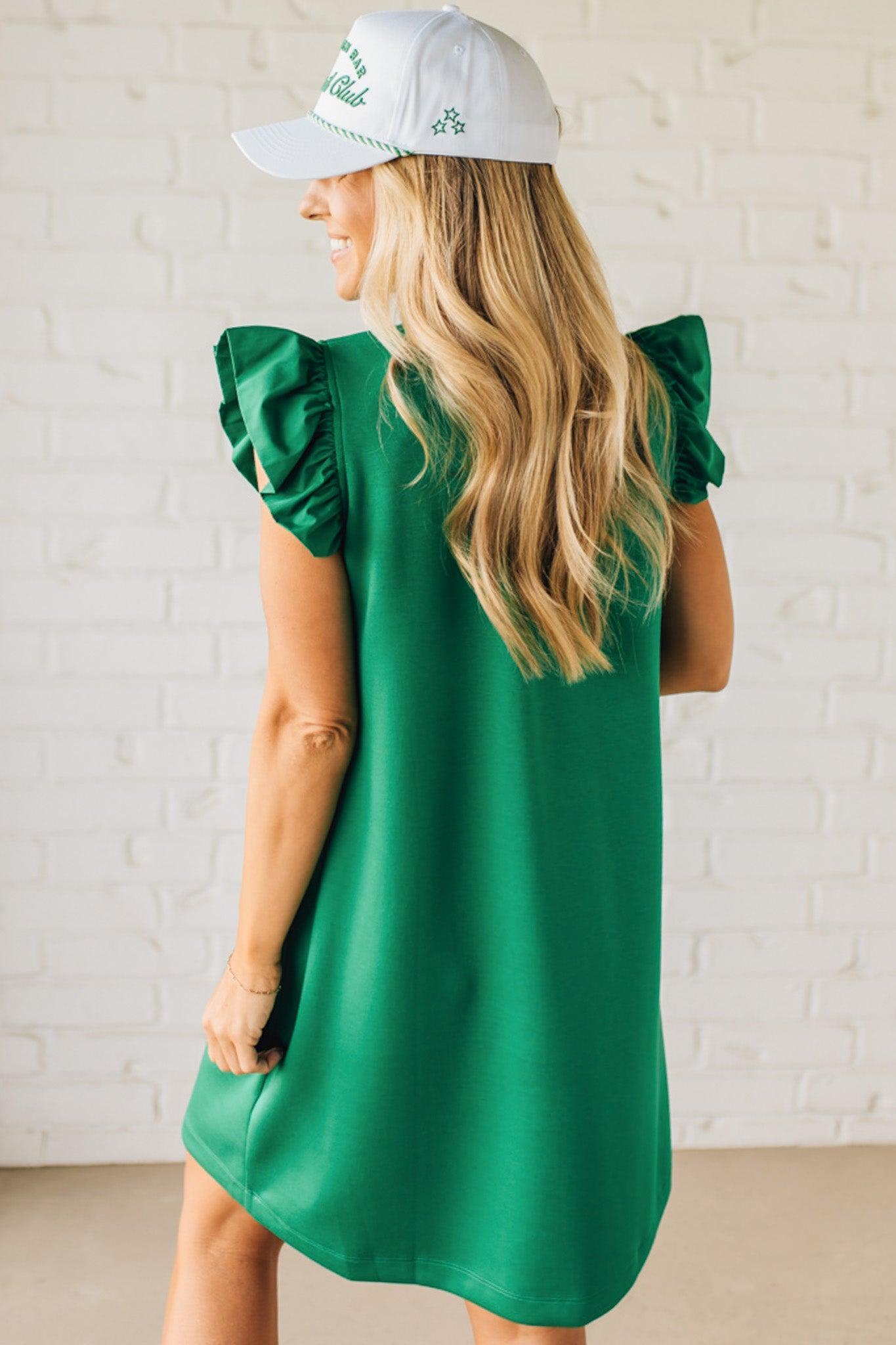 Blonde woman wearing a ruffled cap sleeves shift dress with pockets, ruffled neckline, button detail front pockets, button closure back, in sleek soft fabric.