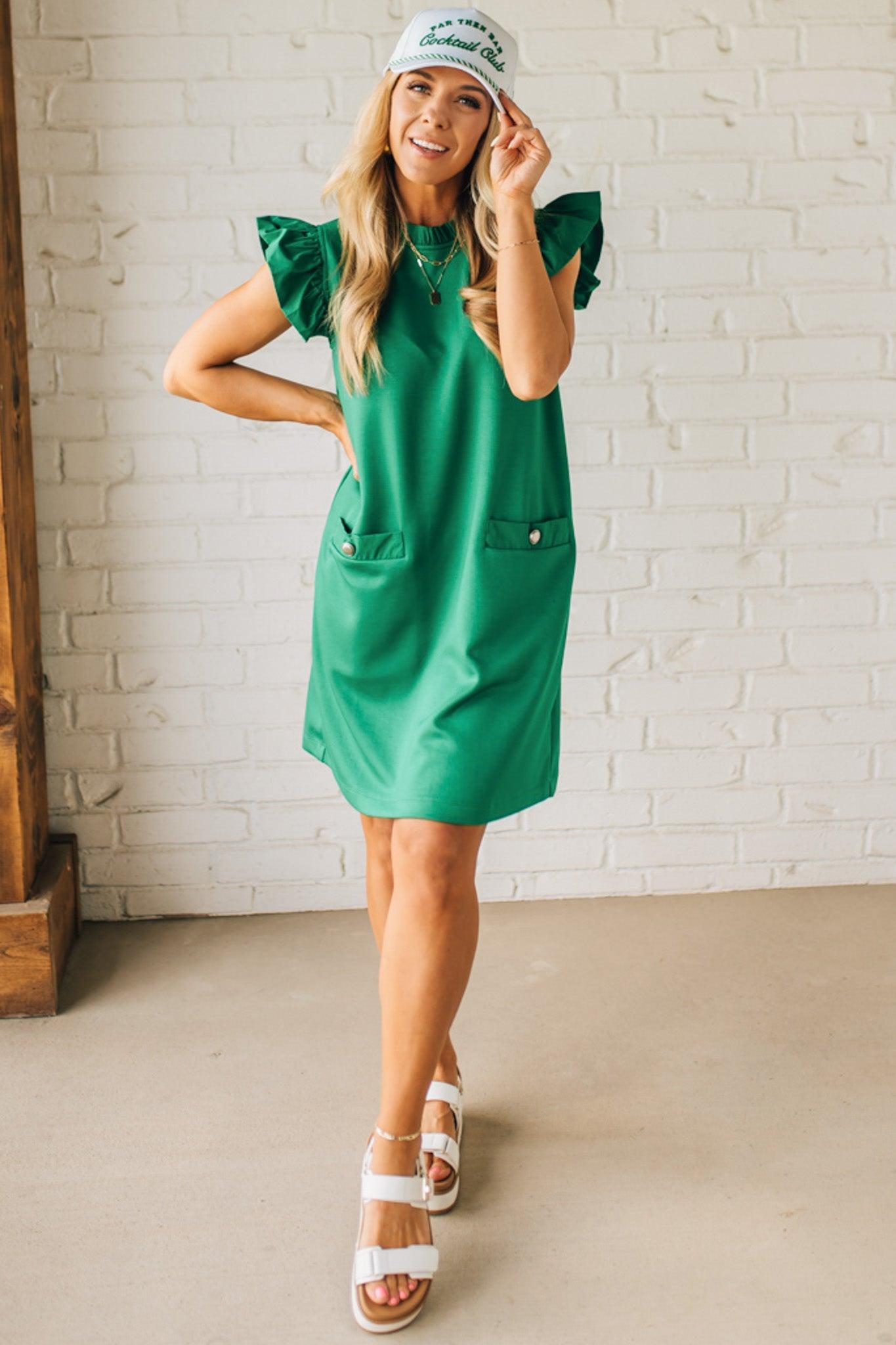 Blonde woman wearing a ruffled cap sleeves shift dress with pockets, ruffled neckline, button detail front pockets, button closure back, in sleek soft fabric.