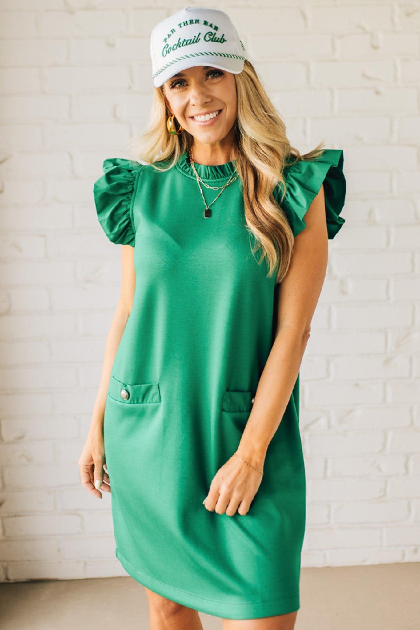 Blonde woman wearing a ruffled cap sleeves shift dress with pockets, ruffled neckline, button detail front pockets, button closure back, in sleek soft fabric.