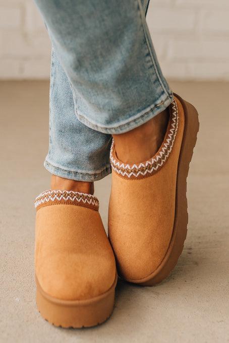 Brown slippers with white trim worn with light blue jeans on a neutral background