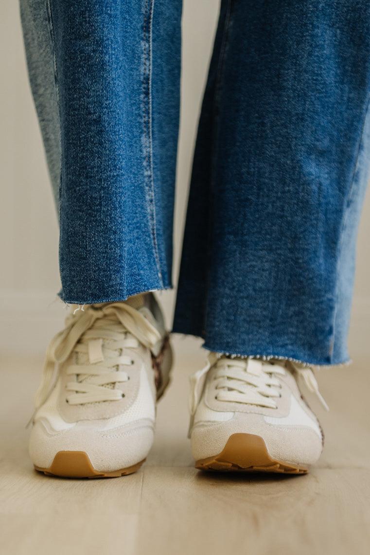 White sneakers with brown soles worn with blue jeans on a neutral background