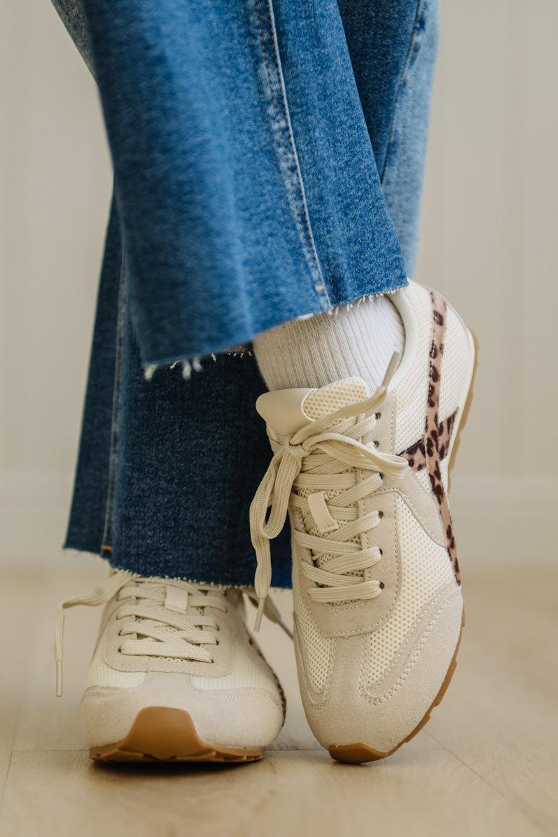 Beige sneakers with brown accents worn with blue jeans and white socks on a neutral background