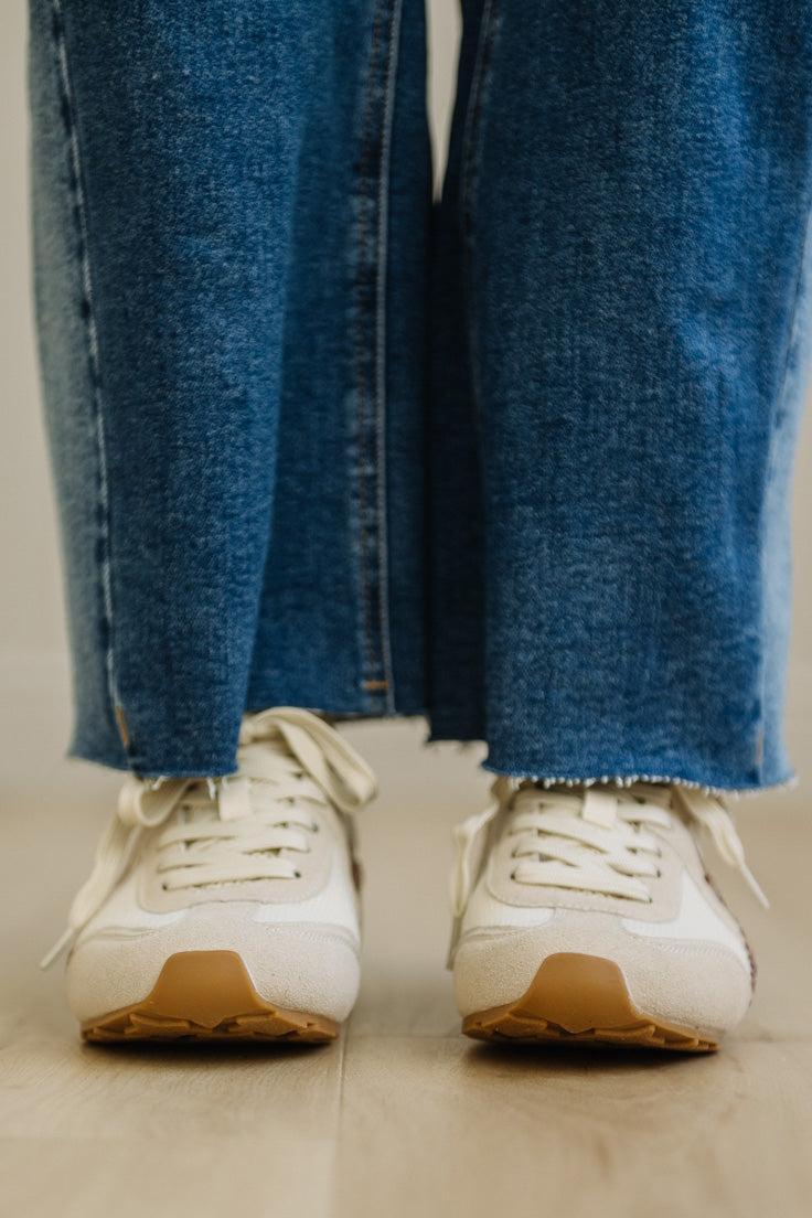 White sneakers with brown soles worn with blue jeans on a light background