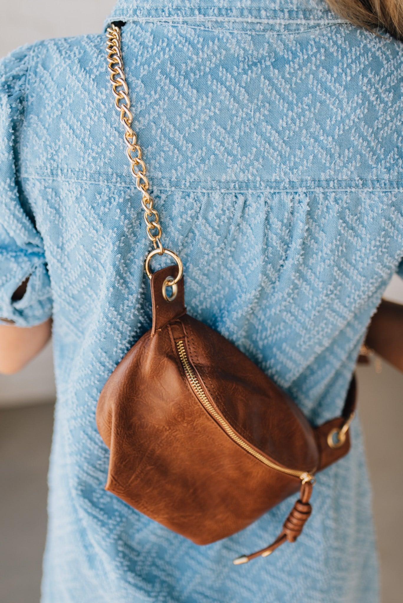Blonde woman wearing a blue denim dress and cognac colored vegan leather crossbody back with gold hardware.