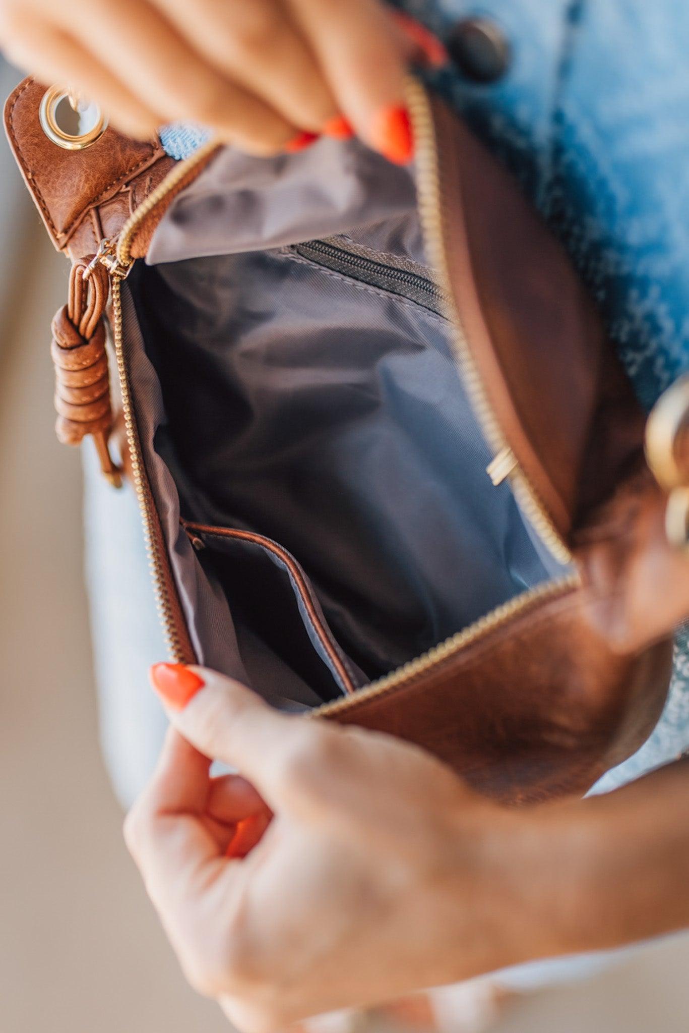 Blonde woman wearing a blue denim dress and cognac colored vegan leather crossbody back with gold hardware.