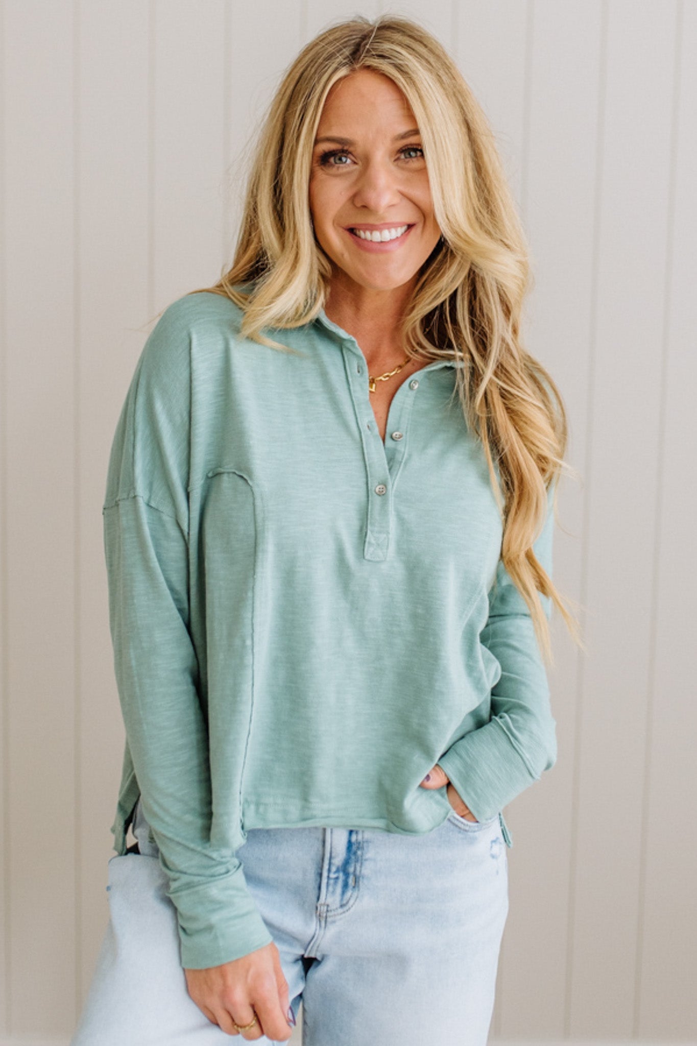 Woman wearing a light green long-sleeve shirt with a zipper, standing against a neutral background.