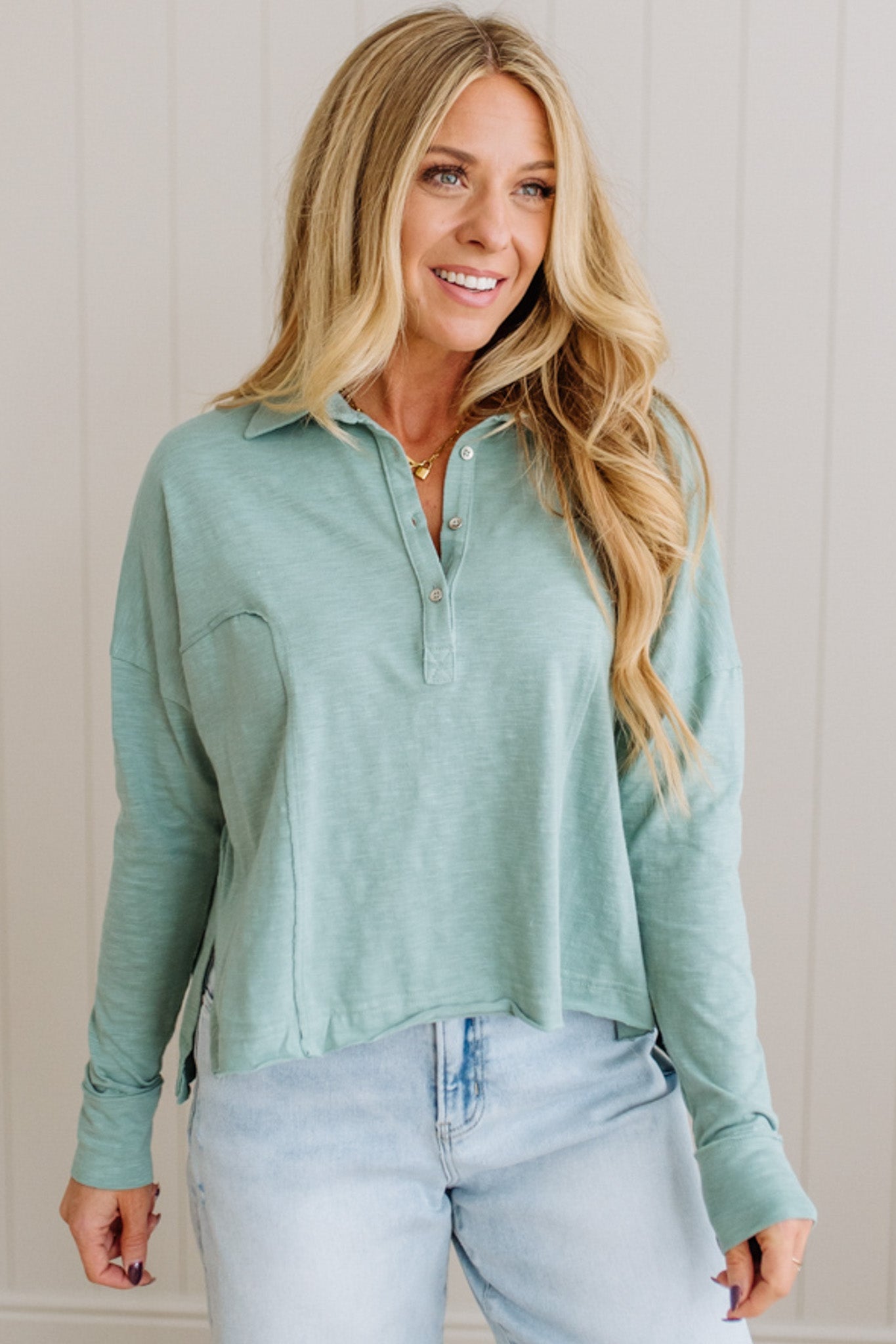 Woman wearing a light green long-sleeve shirt and light blue jeans against a neutral background