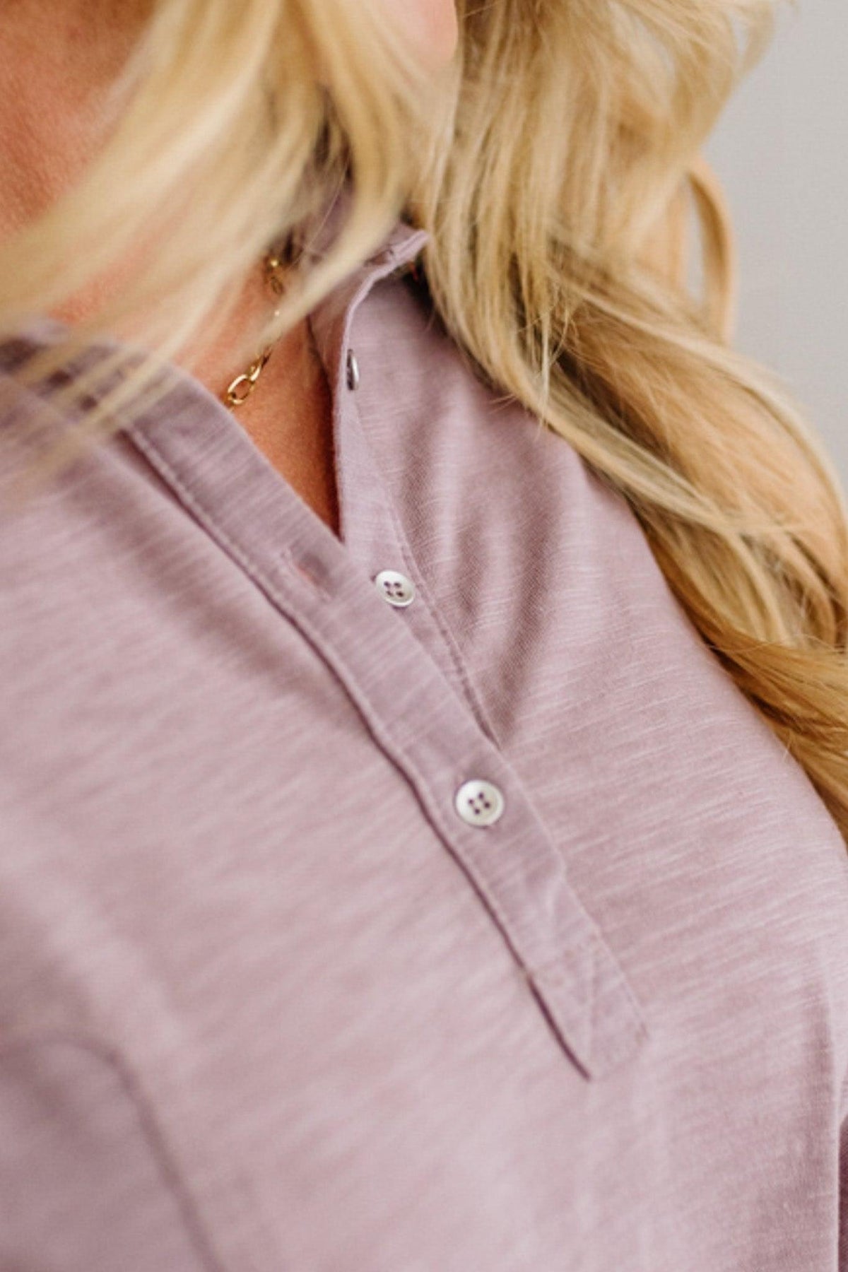 Close-up of a person wearing a light purple shirt with buttons, focusing on the collar area.