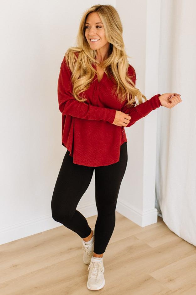 Woman wearing a red top and black leggings standing against a white wall.