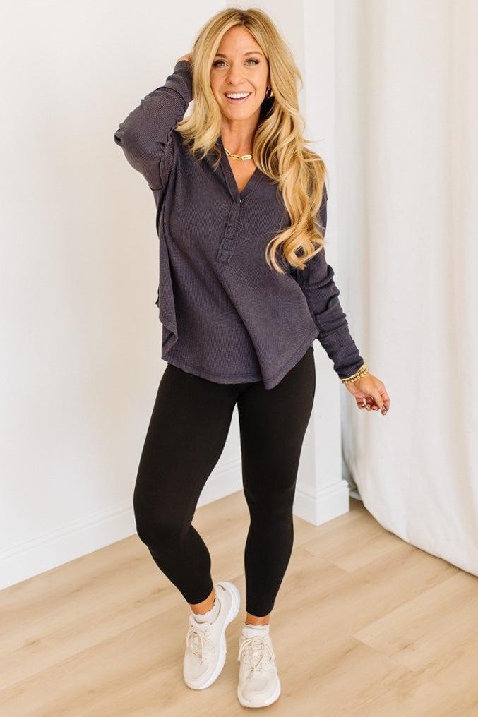 Woman wearing a dark navy long-sleeve shirt and black leggings, standing indoors.