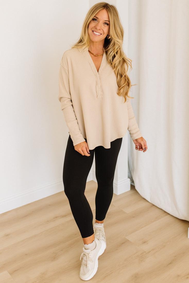 Woman wearing a beige top and black leggings standing in a room with white curtains.
