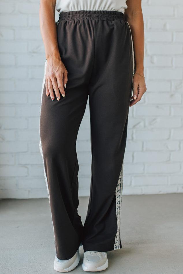 Person wearing black pants with white stripes against a white brick wall.