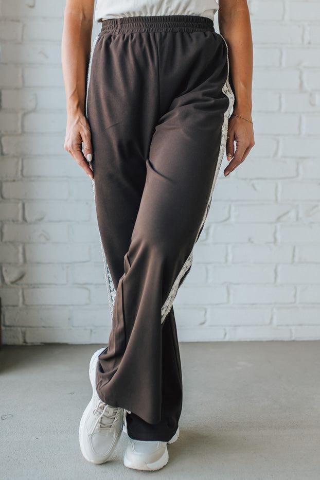 Person wearing brown wide-leg pants and white sneakers against a white brick wall.