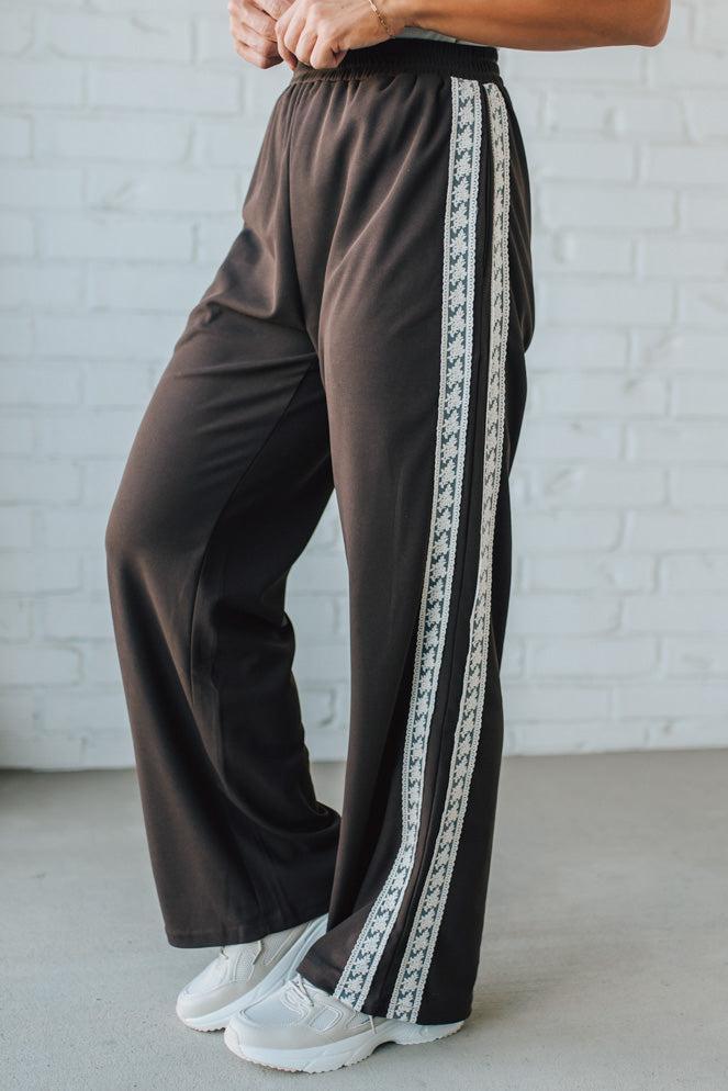 Brown pants with white stripe on a person against a white brick wall.