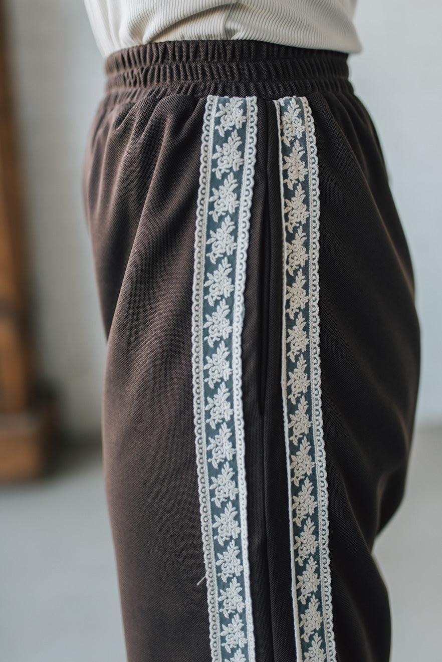 Brown pants with white lace trim worn by a person, against a neutral background.