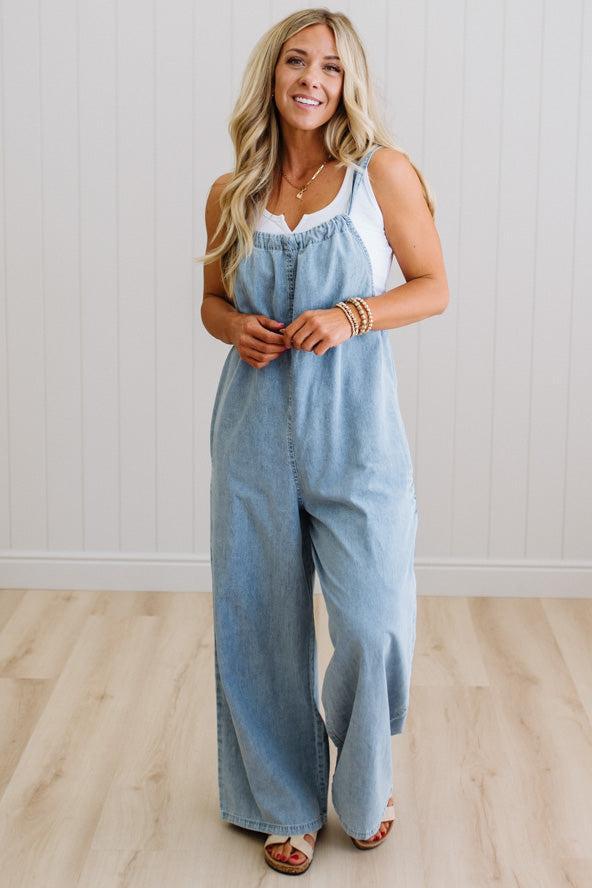 Woman wearing a light blue denim jumpsuit against a white wall.