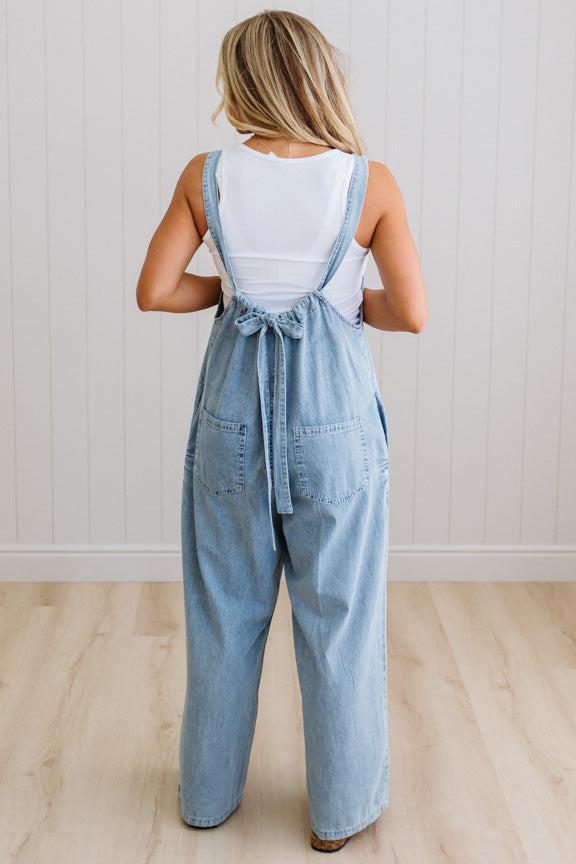 Person wearing a denim overalls with a white top against a light wooden floor and wall background