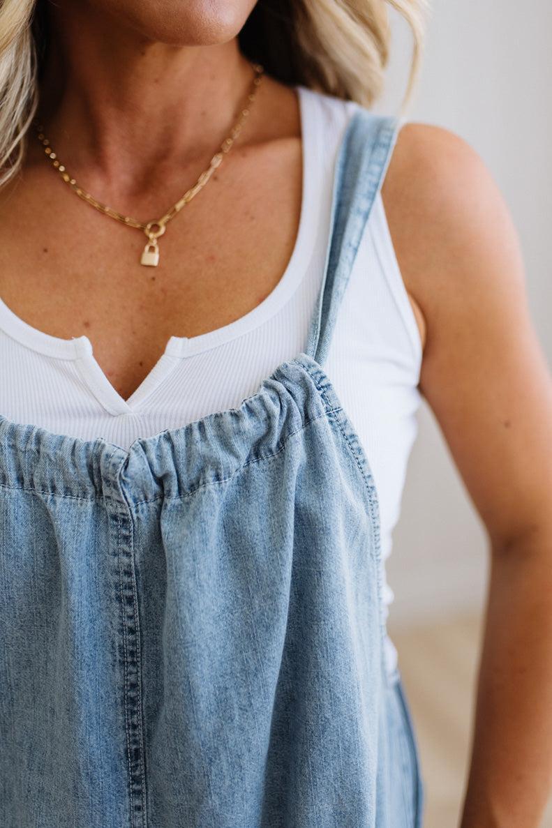 Woman wearing a white tank top and blue denim overalls with a blurred background