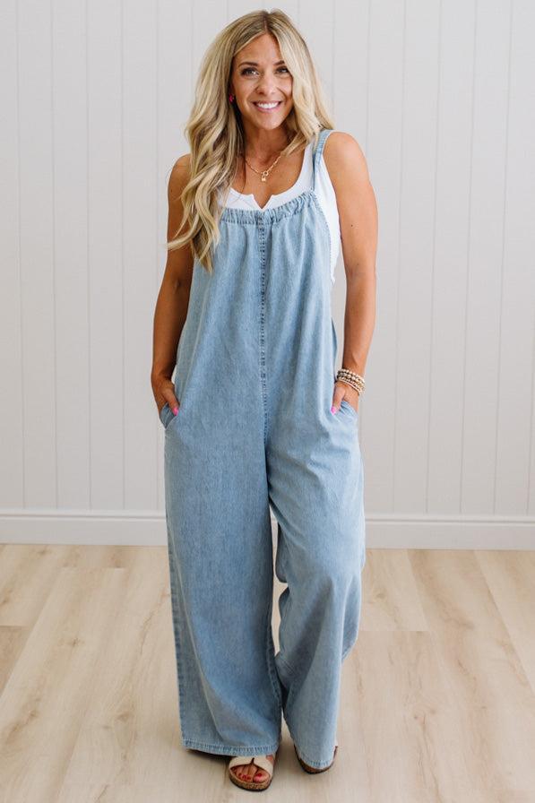 Woman wearing a light blue denim jumpsuit against a white wall.