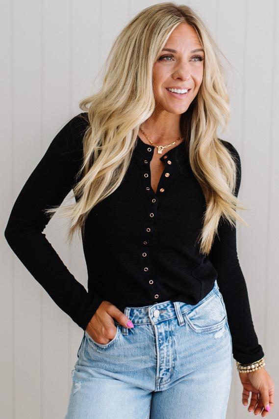 Woman wearing a black long-sleeve top and blue jeans against a plain background
