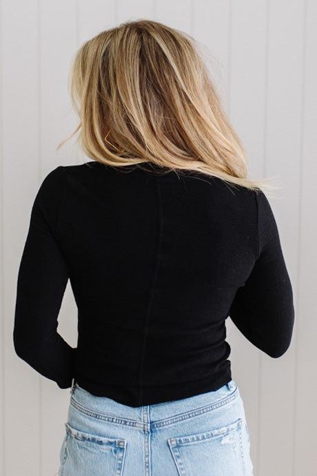 Person wearing a black long-sleeve top and light blue jeans against a white wall.