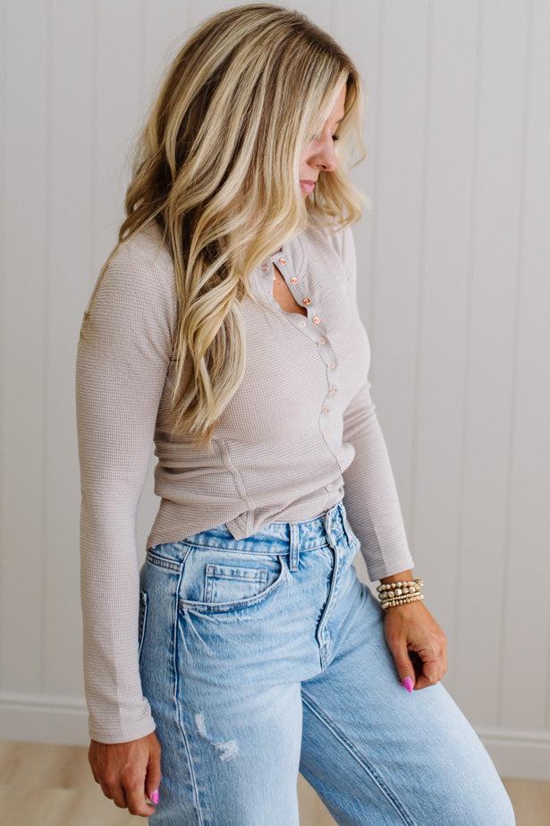 Woman wearing a beige long-sleeve top and light blue jeans against a neutral background