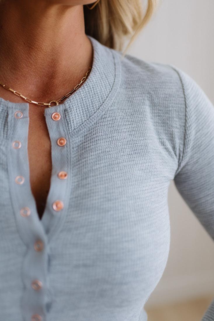 Close-up of a person wearing a light blue ribbed sweater with pink buttons.