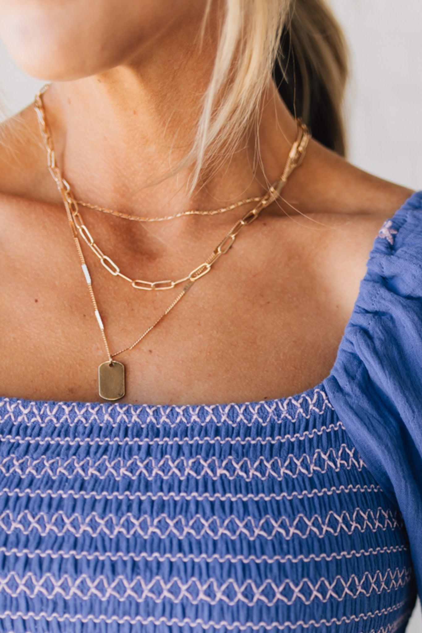 Three strand gold necklace with different chains, and one tag charm.