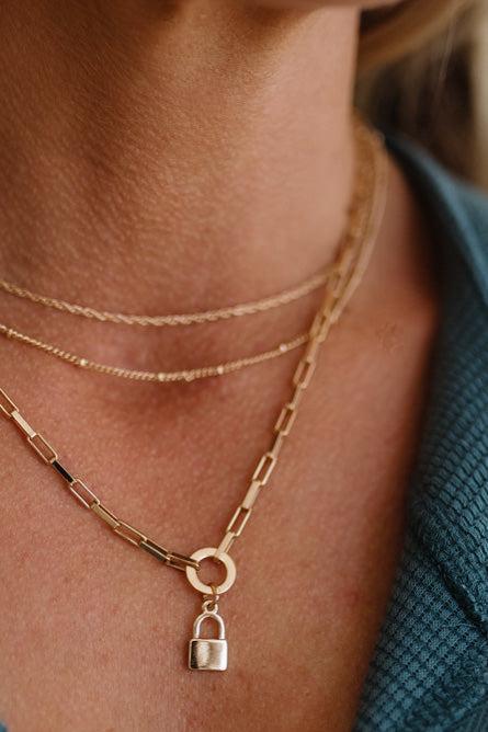 Close-up of a person wearing a gold chain necklace with a lock pendant.