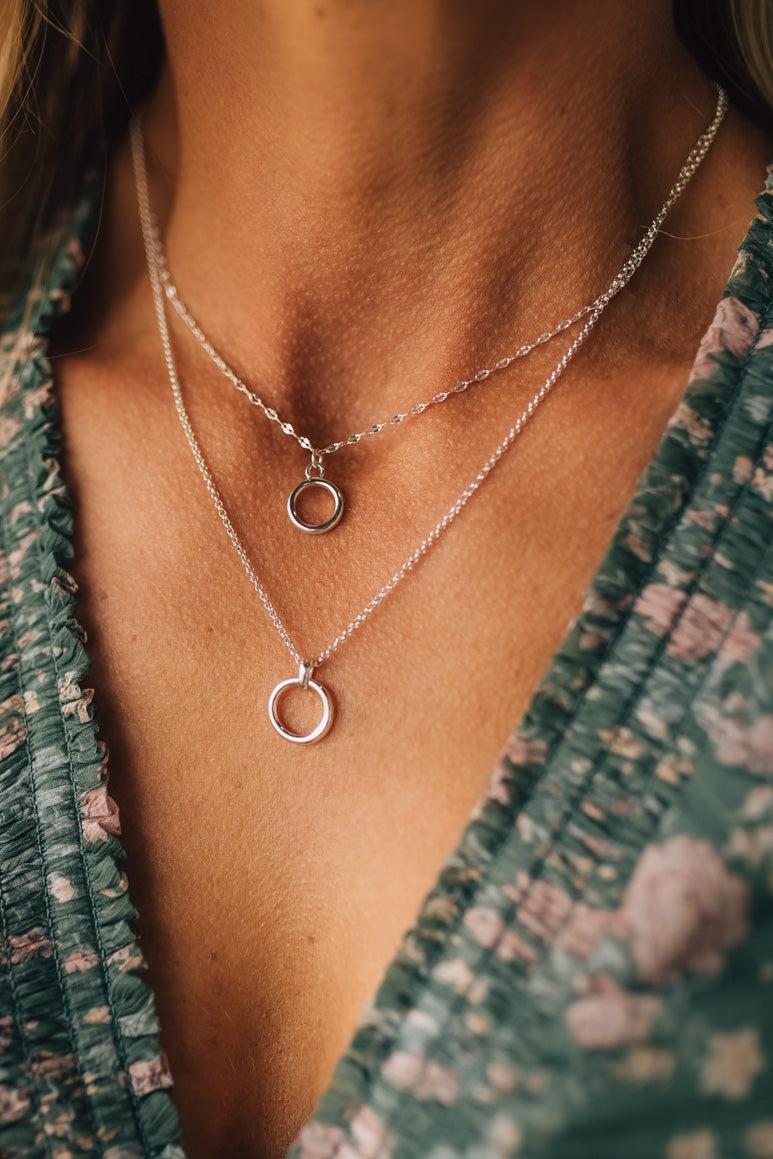 Close-up of a person wearing two silver necklaces with circular pendants.
