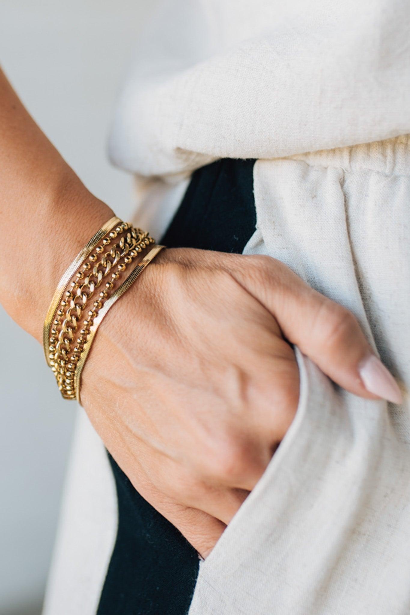 Hand wearing a gold bracelet with a neutral background
