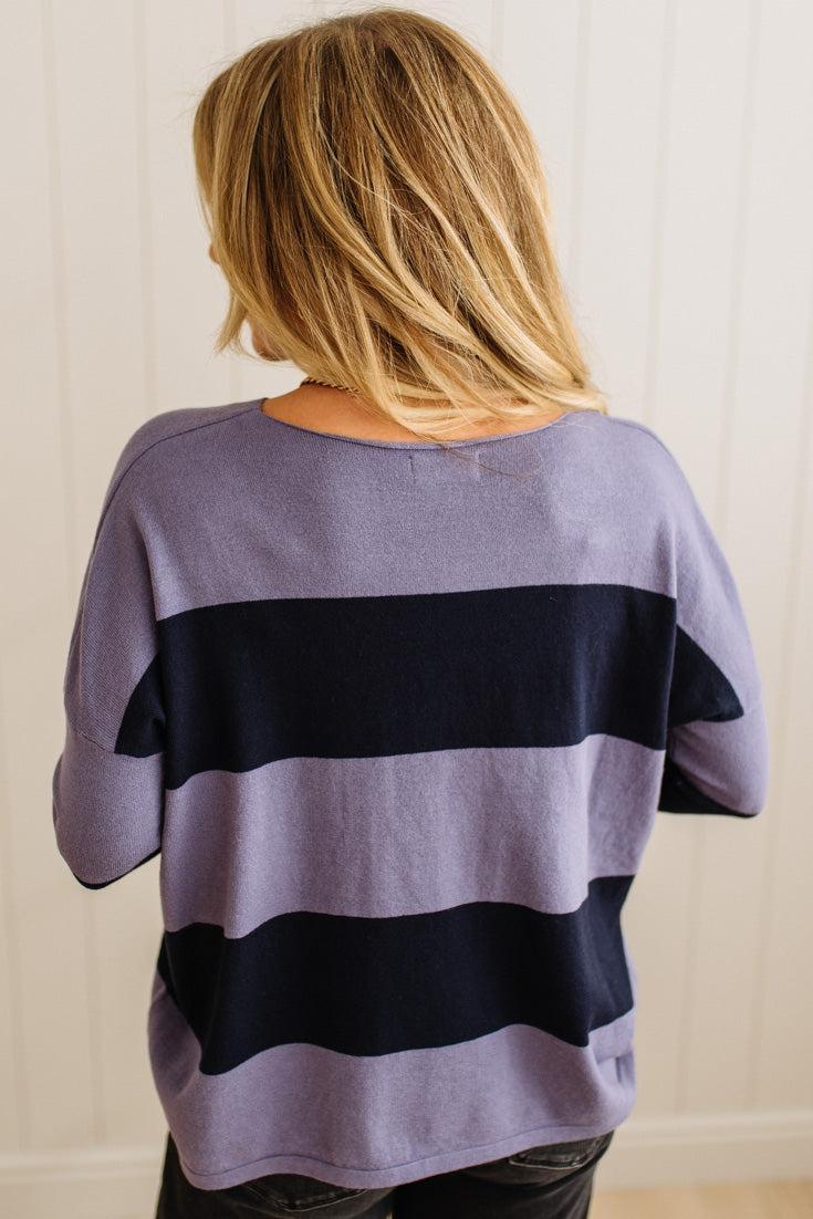 Person wearing a purple and navy striped sweater against a plain background