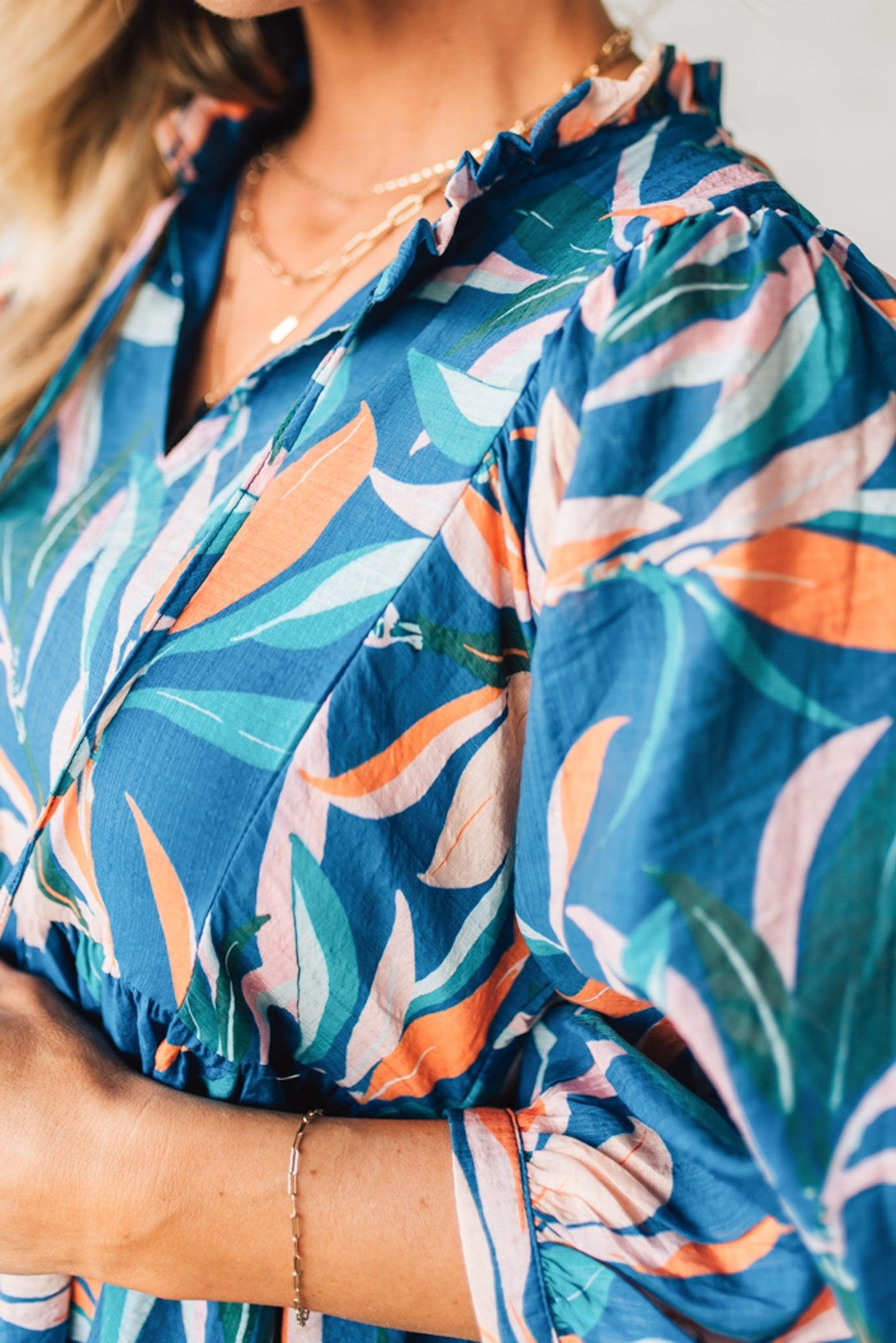 Blonde woman wearing a 3/4 sleeves leaf print dress with front tie neck detail, ruffled neckline, side pockets.
