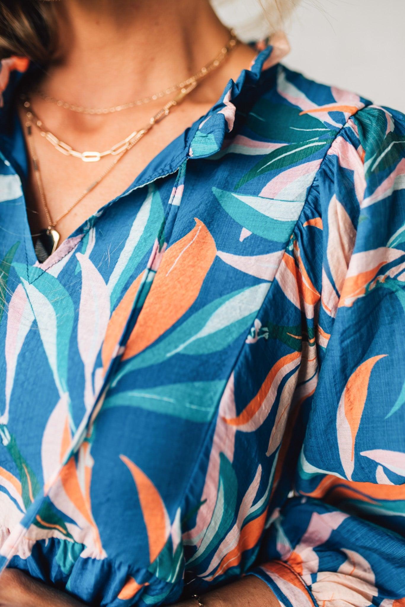 Blonde woman wearing a 3/4 sleeves leaf print dress with front tie neck detail, ruffled neckline, side pockets.