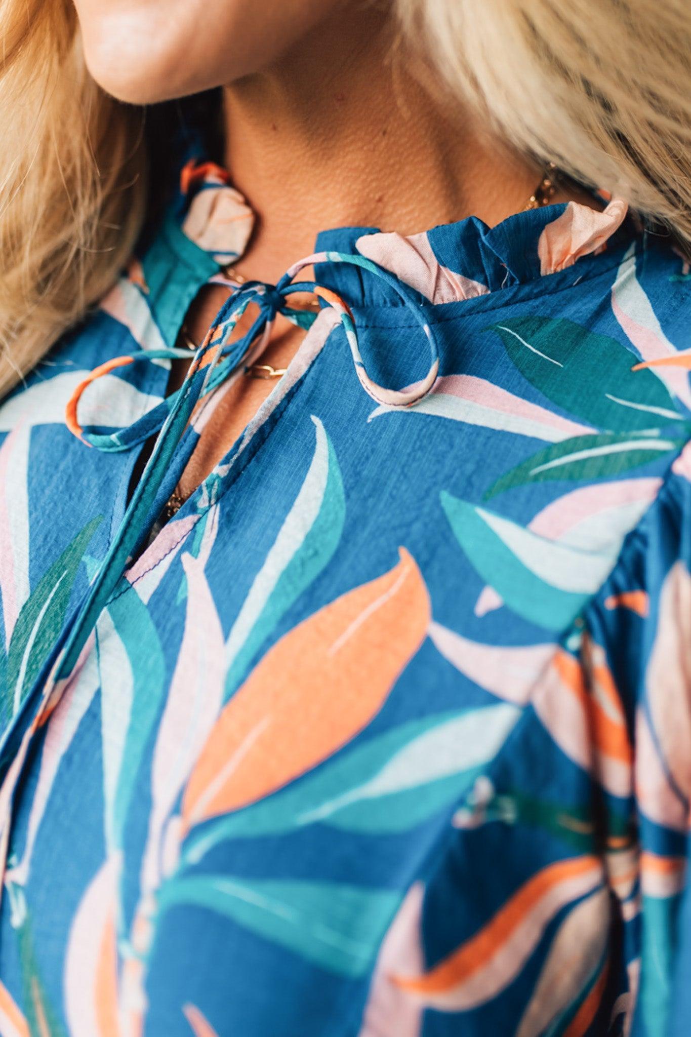 Blonde woman wearing a 3/4 sleeves leaf print dress with front tie neck detail, ruffled neckline, side pockets.