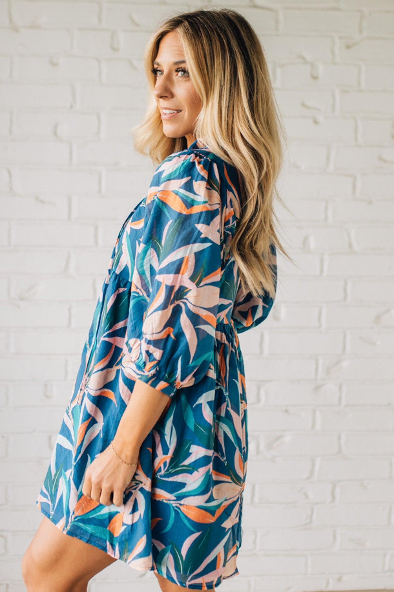 Blonde woman wearing a 3/4 sleeves leaf print dress with front tie neck detail, ruffled neckline, side pockets.