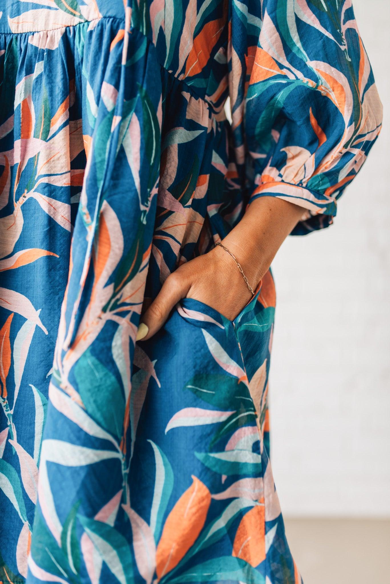 Blonde woman wearing a 3/4 sleeves leaf print dress with front tie neck detail, ruffled neckline, side pockets.