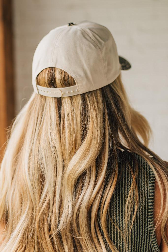 Blonde woman wearing a cream colored trucker hat with leopard print brim, and gold TEXAS embroidered at the front.