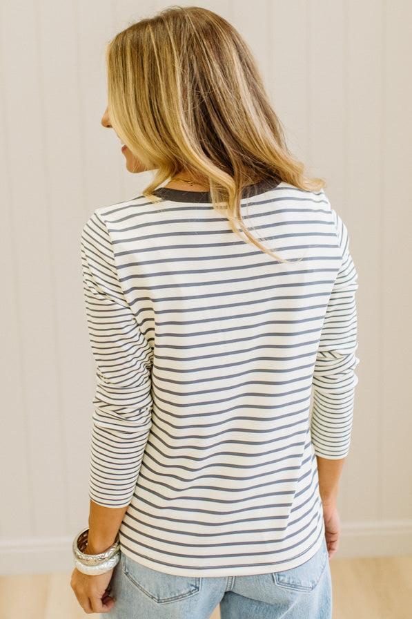 Blonde woman in a brightly lit studio wearing light wide leg jeans, dark clogs, and a striped henley top in cream and charcoal.