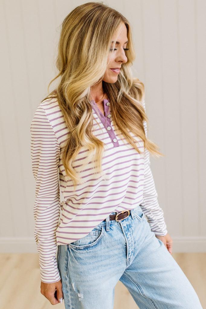 Blonde woman in a brightly lit studio wearing light wide leg jeans, dark clogs, and a striped henley top in cream and lavender.