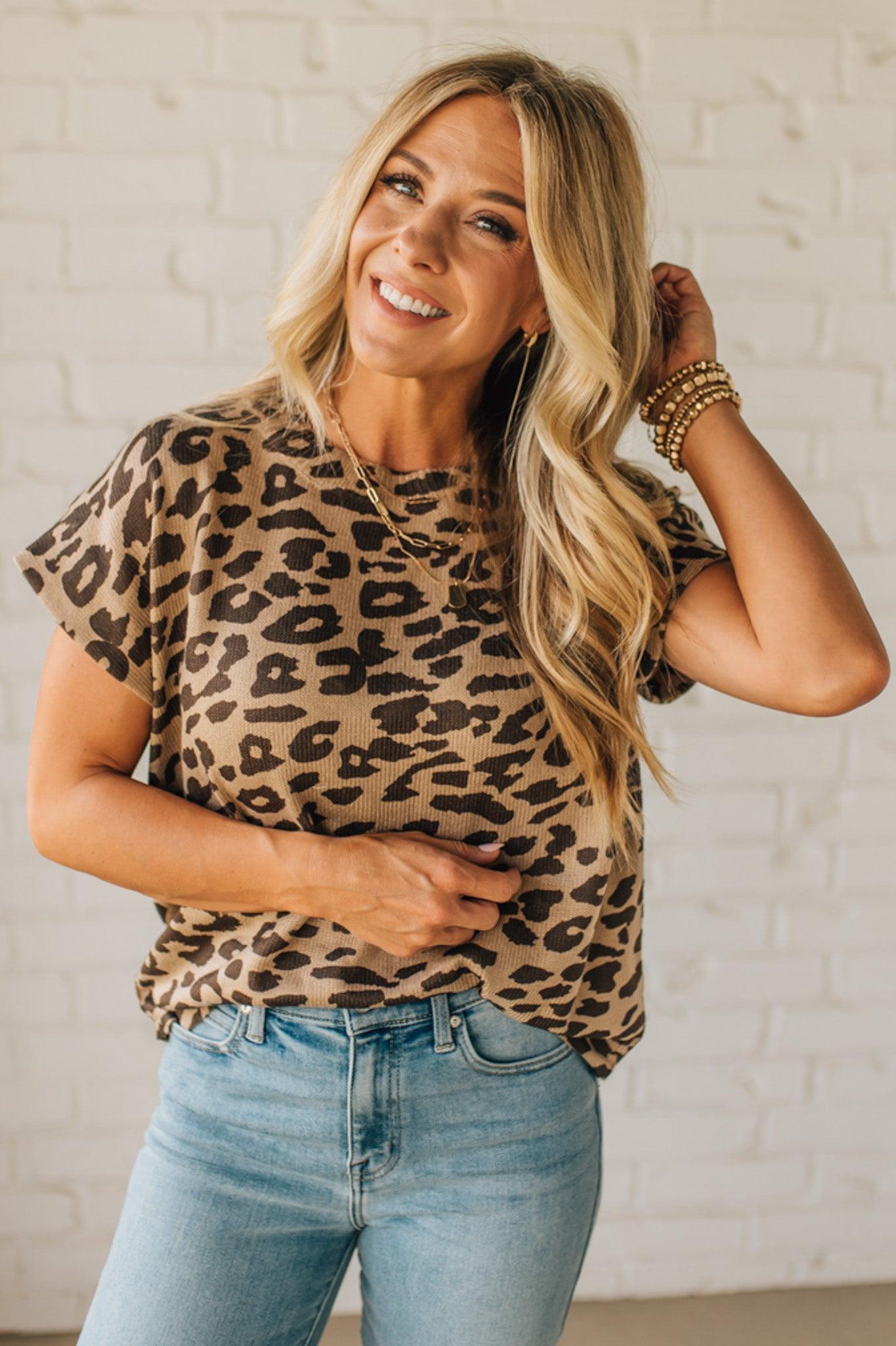 Woman wearing a leopard print top and blue jeans against a white brick wall.