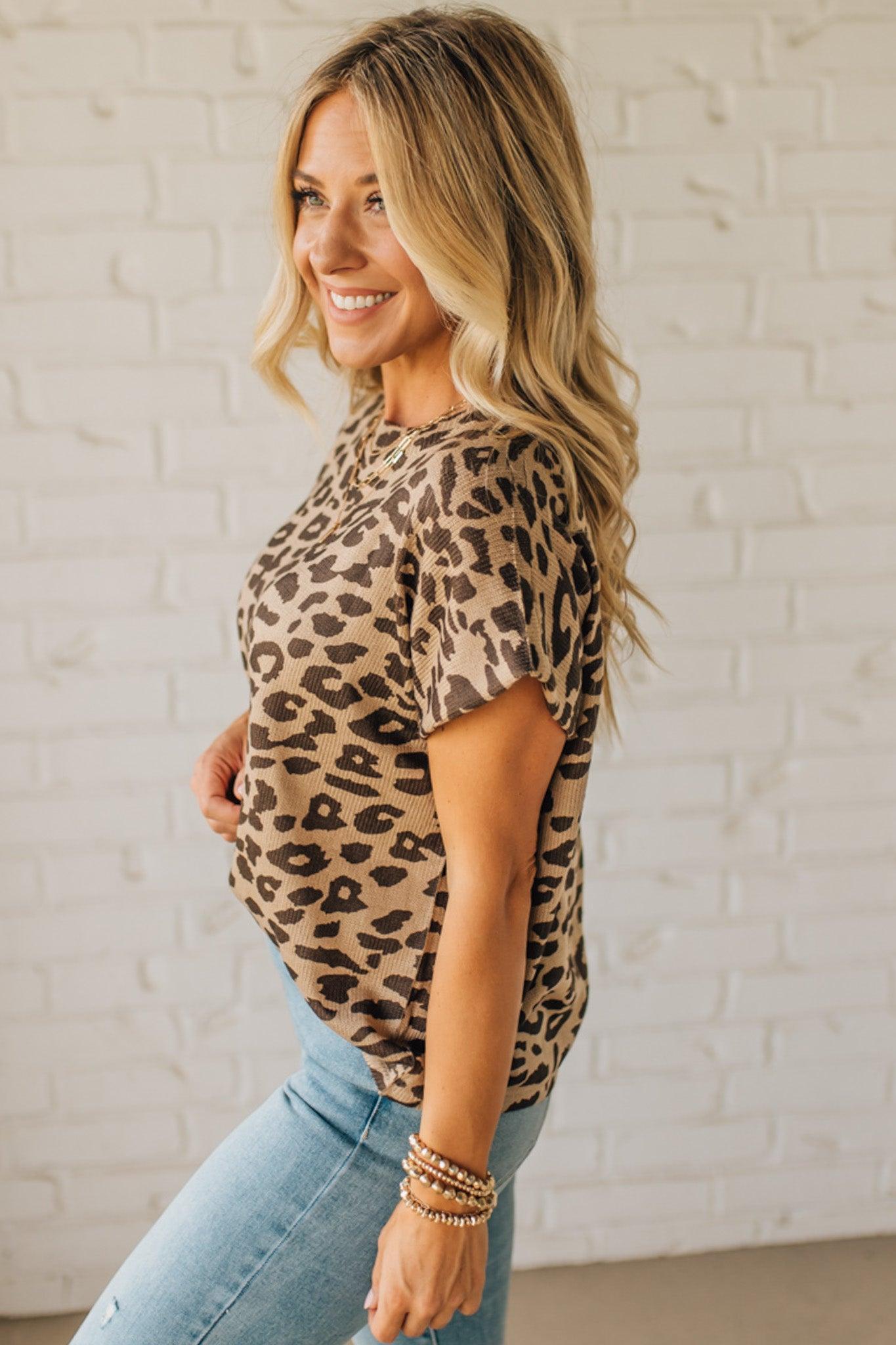 Woman wearing a leopard print top and blue jeans against a white brick wall.
