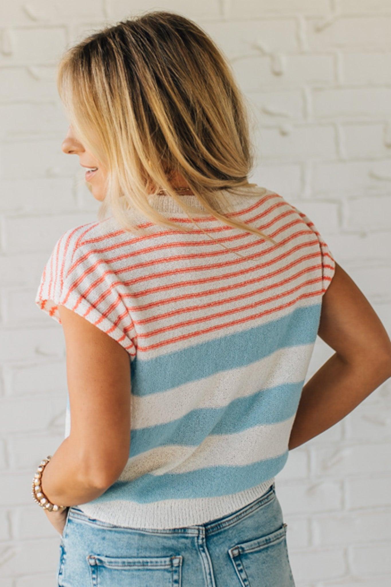BLONDE WOMAN WEARING A STRIPED LIGHTWEIGHT SLEEVELESS DROP SHOULDER SUMMER SWEATER TOP IN RED WHITE AND BLUE.
